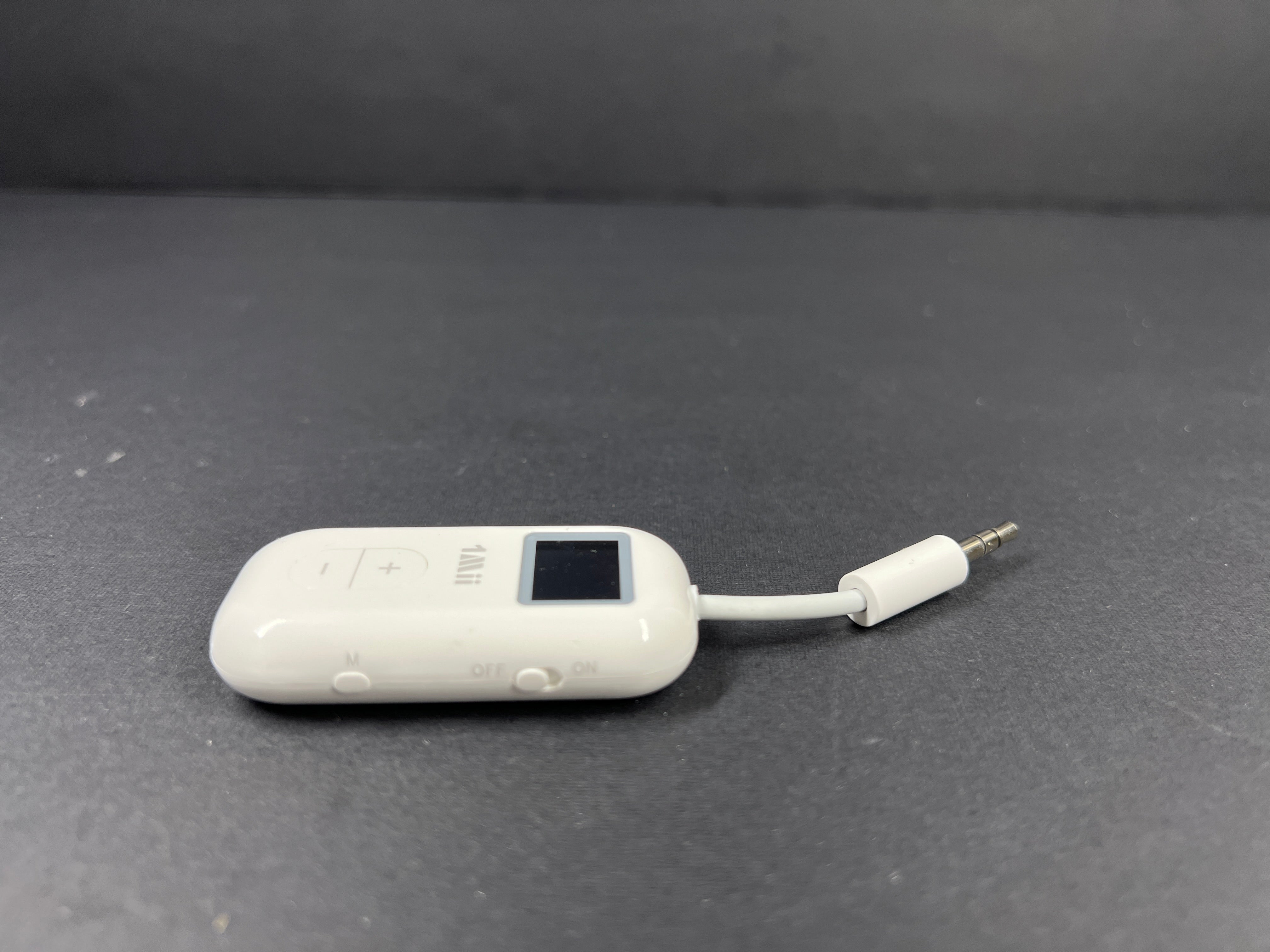 Small white Bluetooth audio adapter with display and 3.5mm jack designed for wireless headphone use on planes