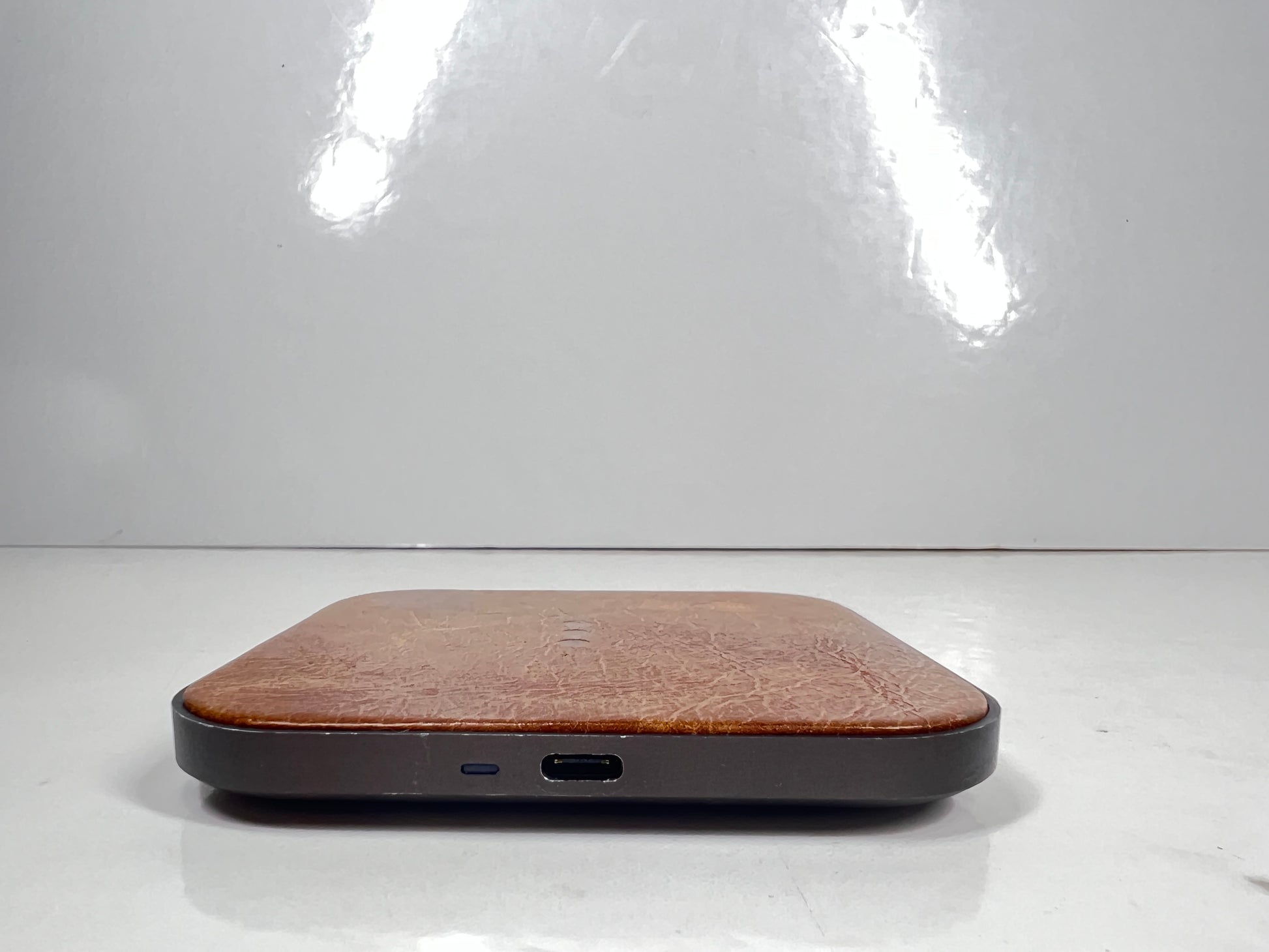 Leather-top Courant wireless charging pad with USB-C input, brown with visible wear and LED indicator dots.
