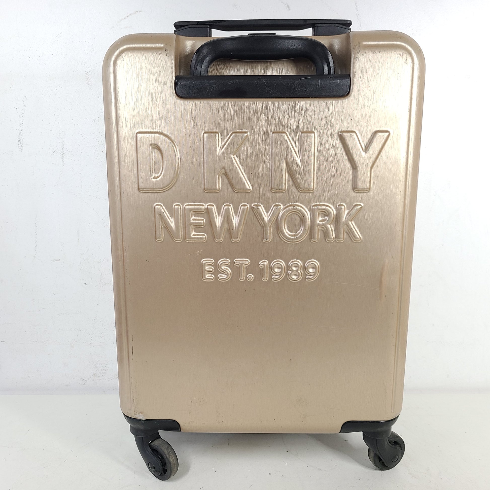 Gold DKNY suitcase with minor surface scratches and a clean interior, branded DKNY NEW YORK EST.1989.