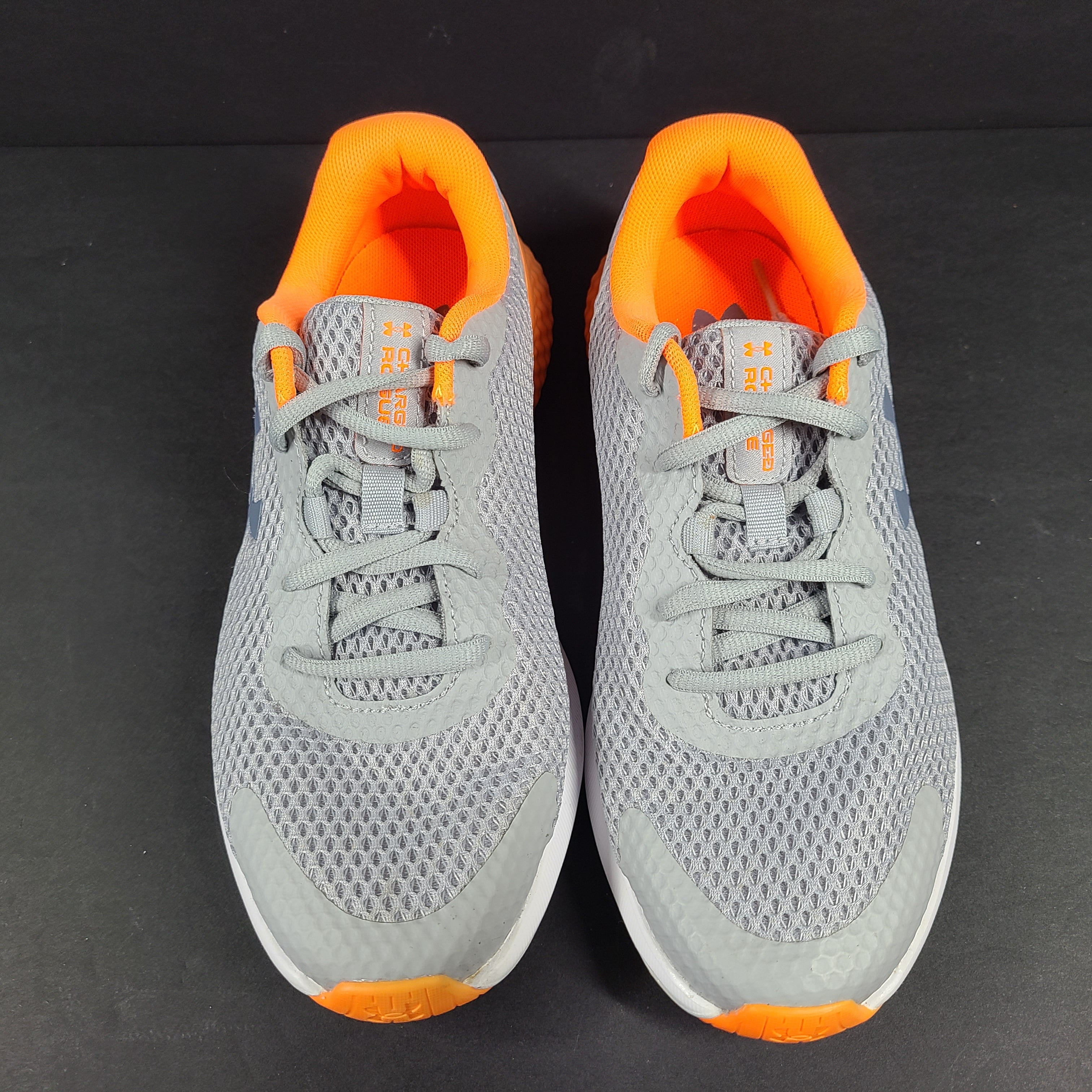 Under Armour Charged Rogue youth running shoes in gray with orange accents and a low-profile silhouette.
