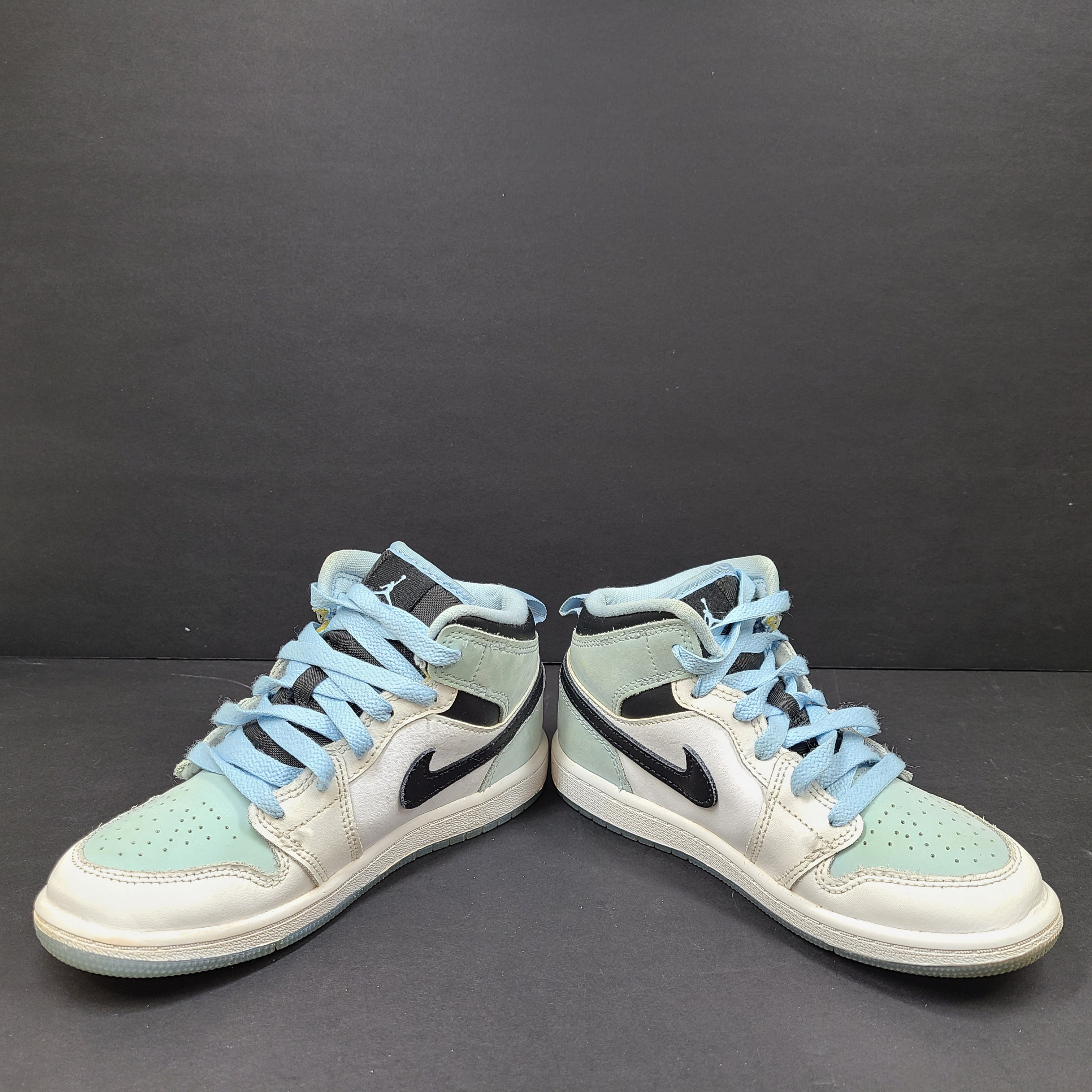 Nike Air Jordan 1 Mid in ice blue, white and black for kids US 13C with mid-top silhouette and modest sole wear.