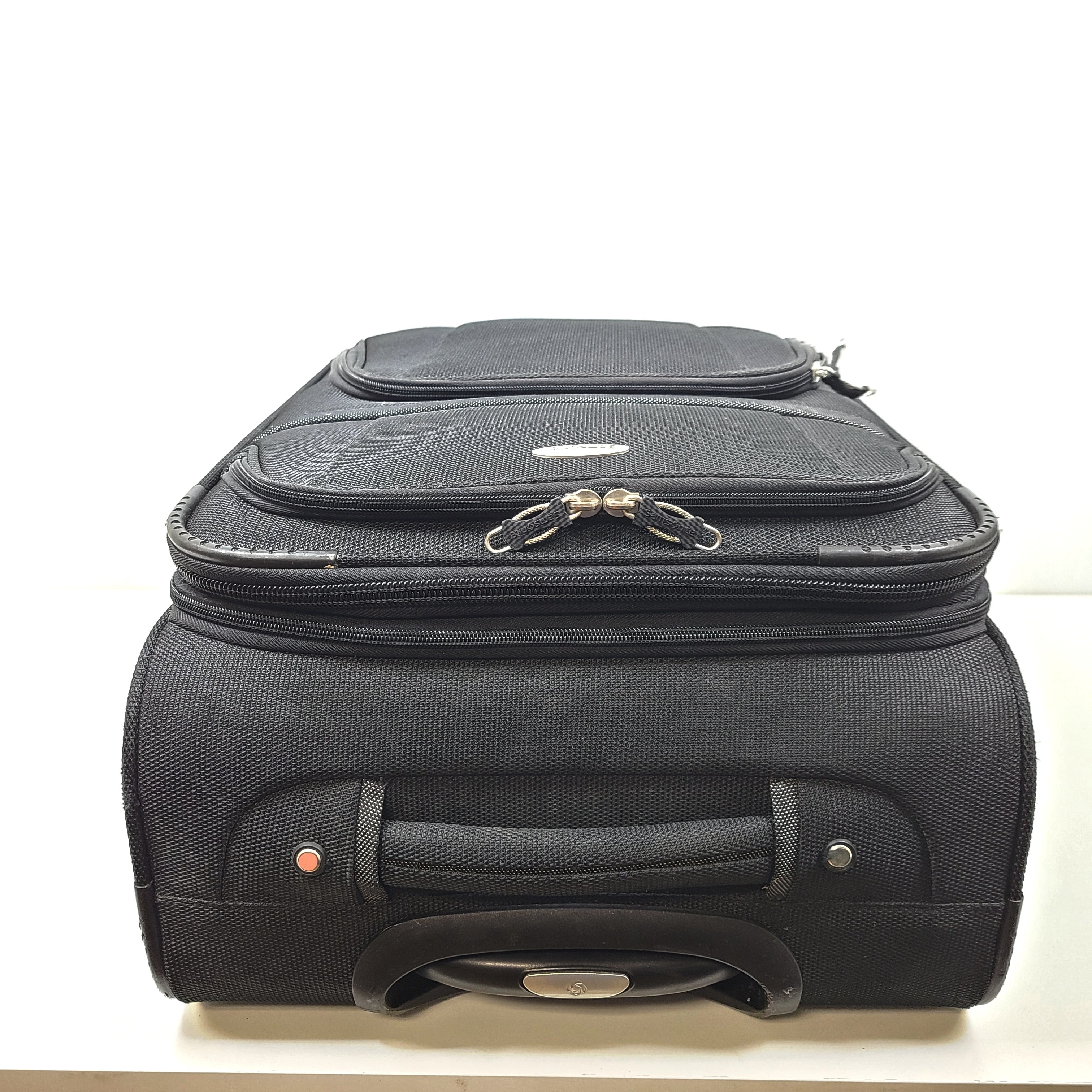 Black Samsonite suitcase QC-002454 with minor scuff marks and labeled material composition.