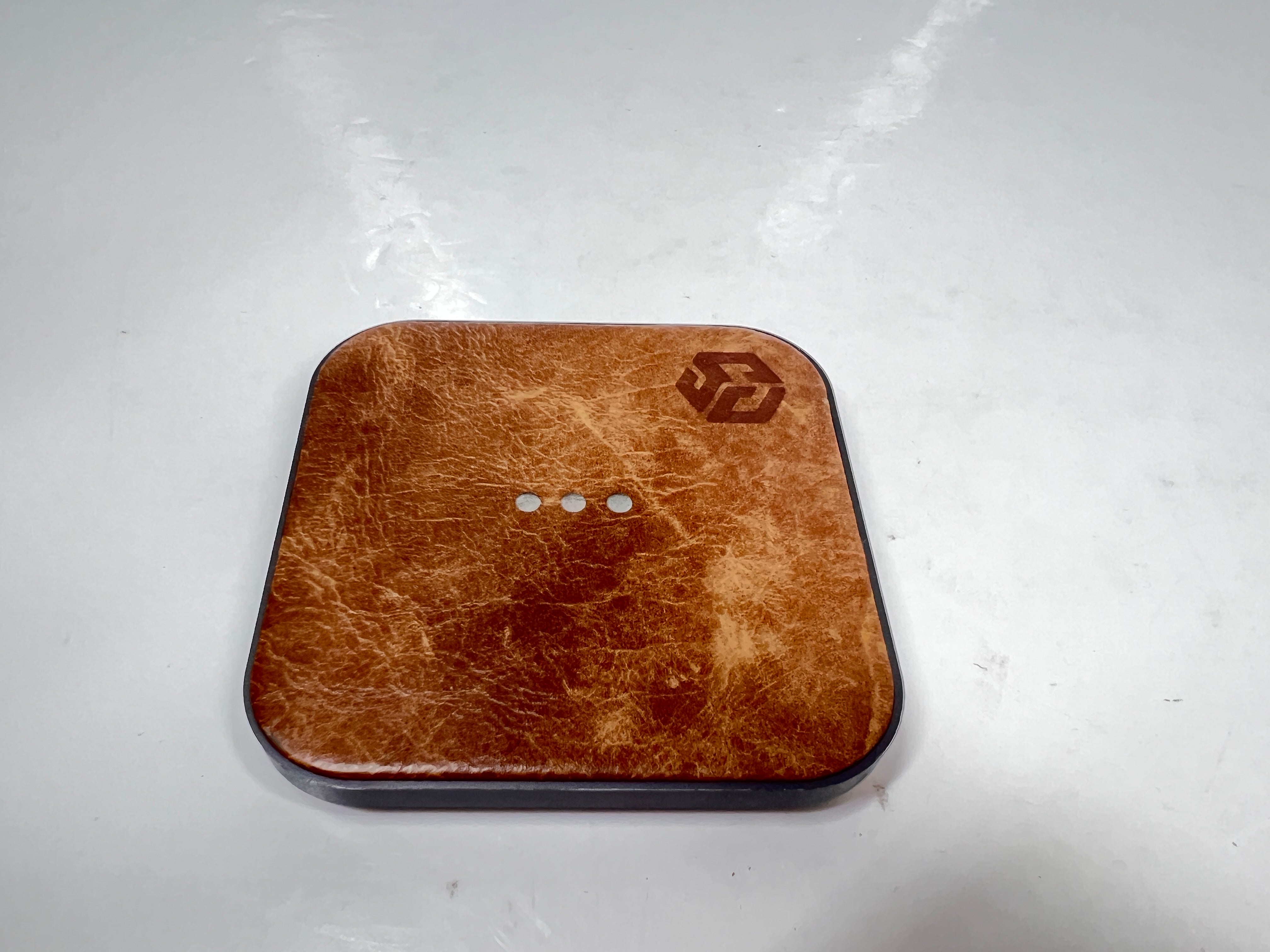 Leather-top Courant wireless charging pad with USB-C input, brown with visible wear and LED indicator dots.