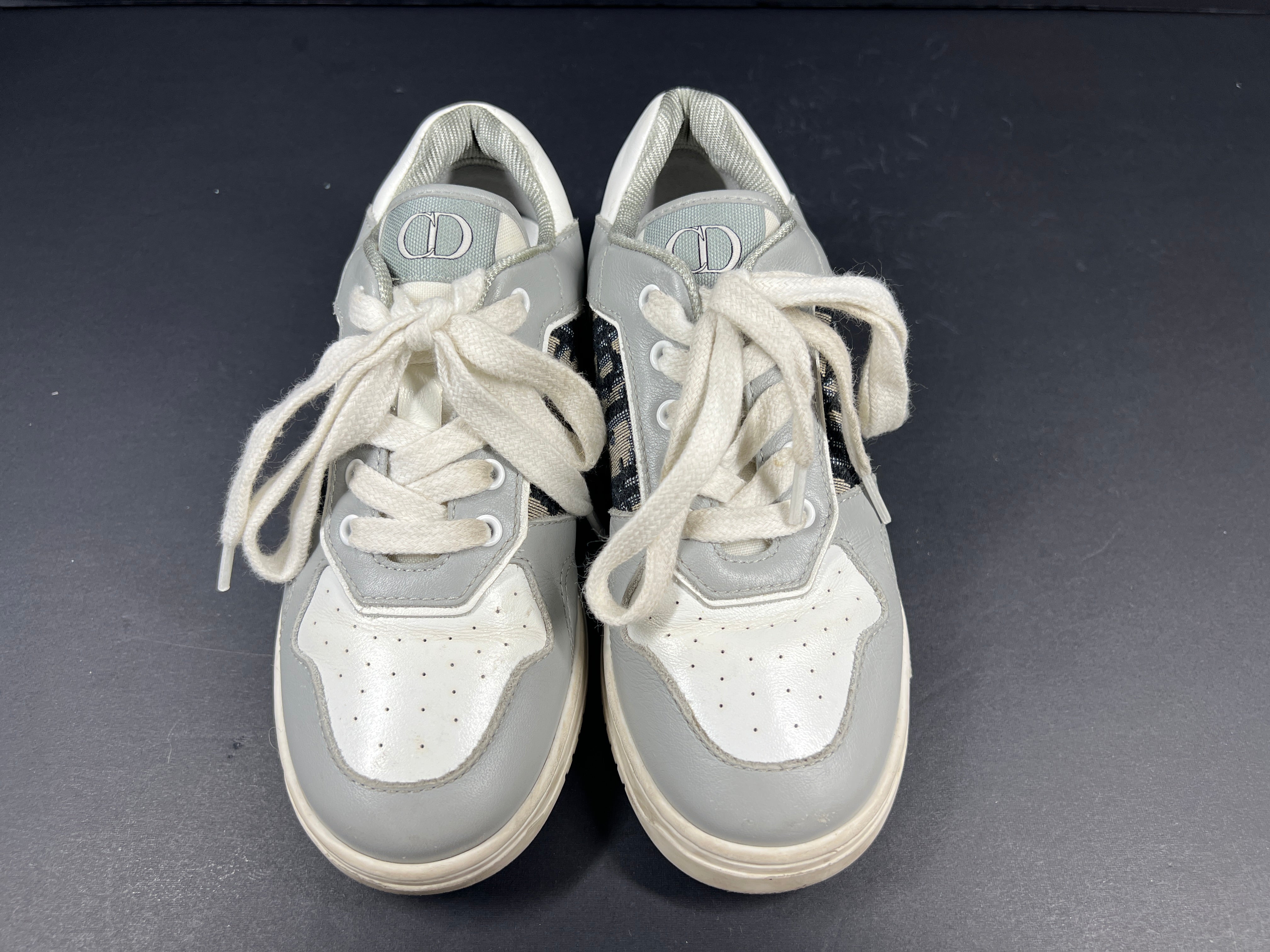A pair of fashionable grey and white Dior women's sneakers.
