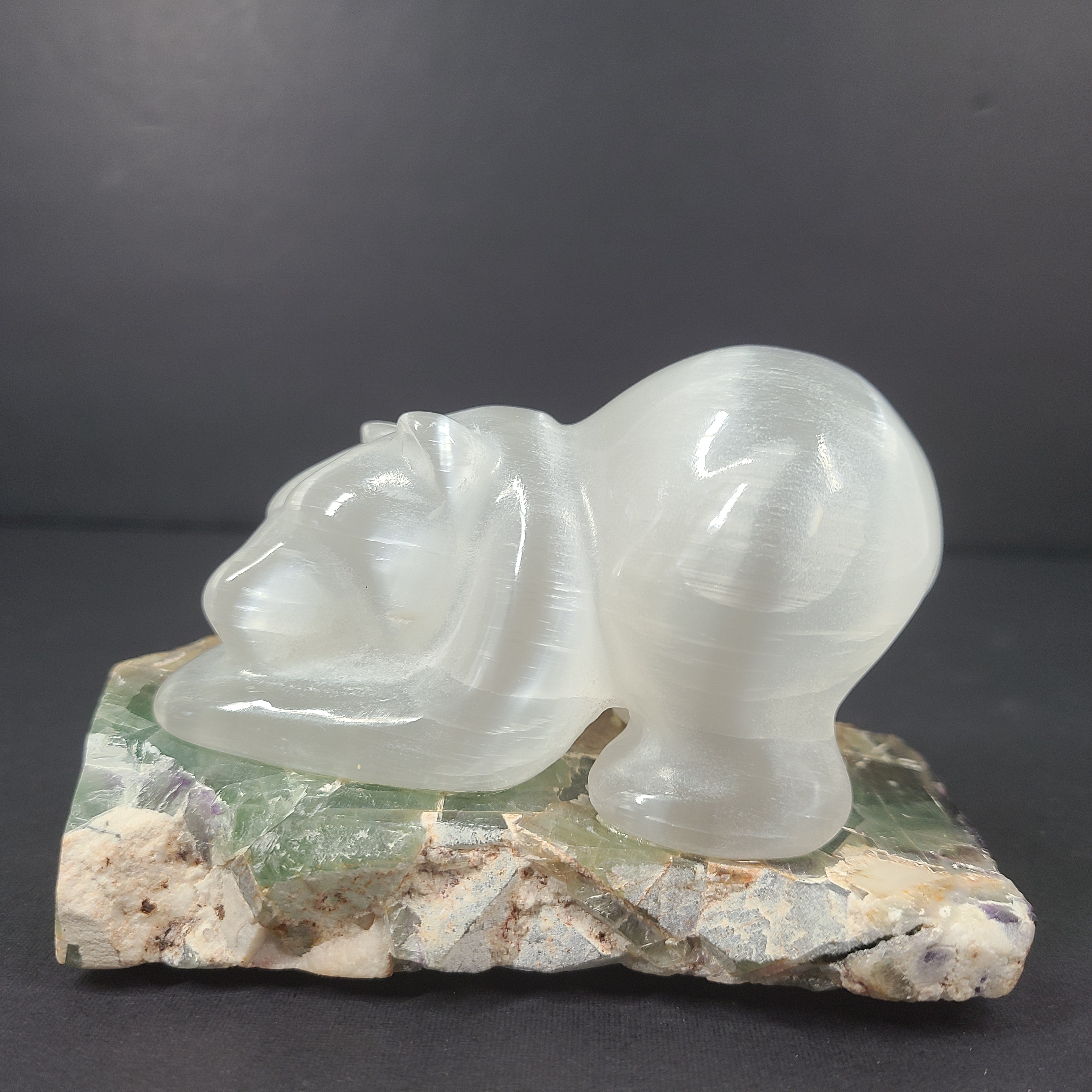 A beautifully hand-carved crystal bear sculpture resting on a stone base.
