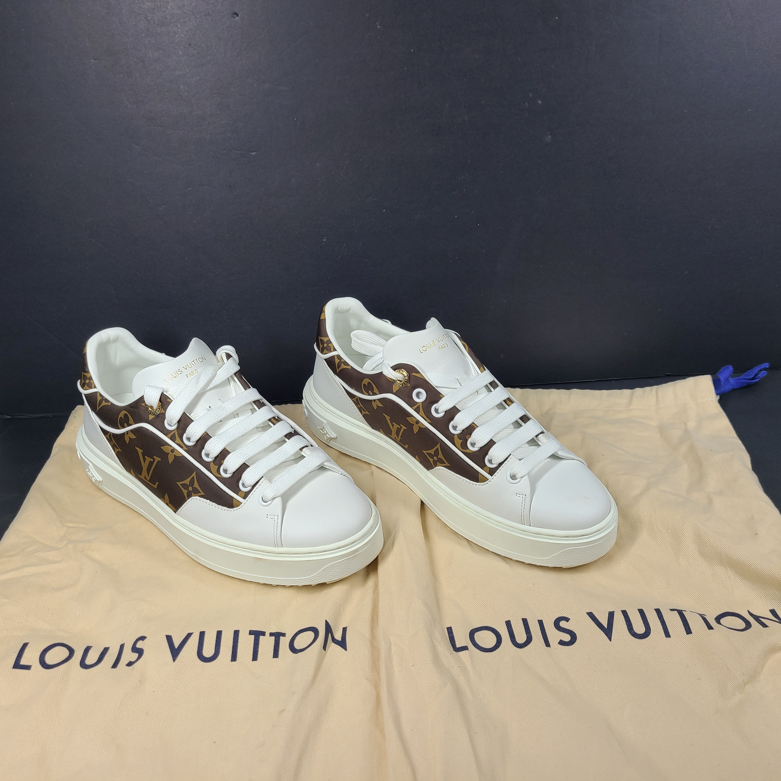 A pair of Louis Vuitton LV Monogram sneakers in white and brown.