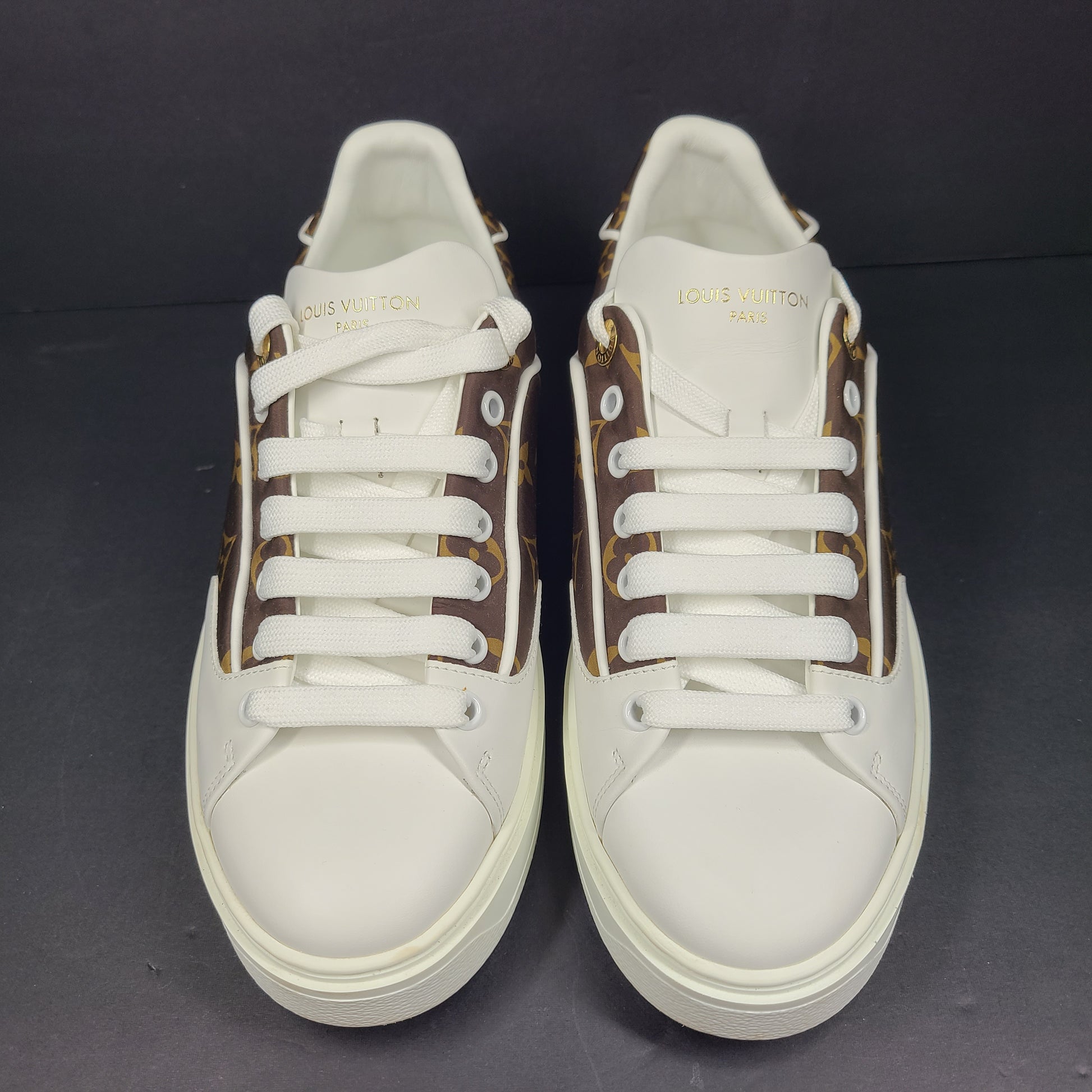 A pair of Louis Vuitton LV Monogram sneakers in white and brown.