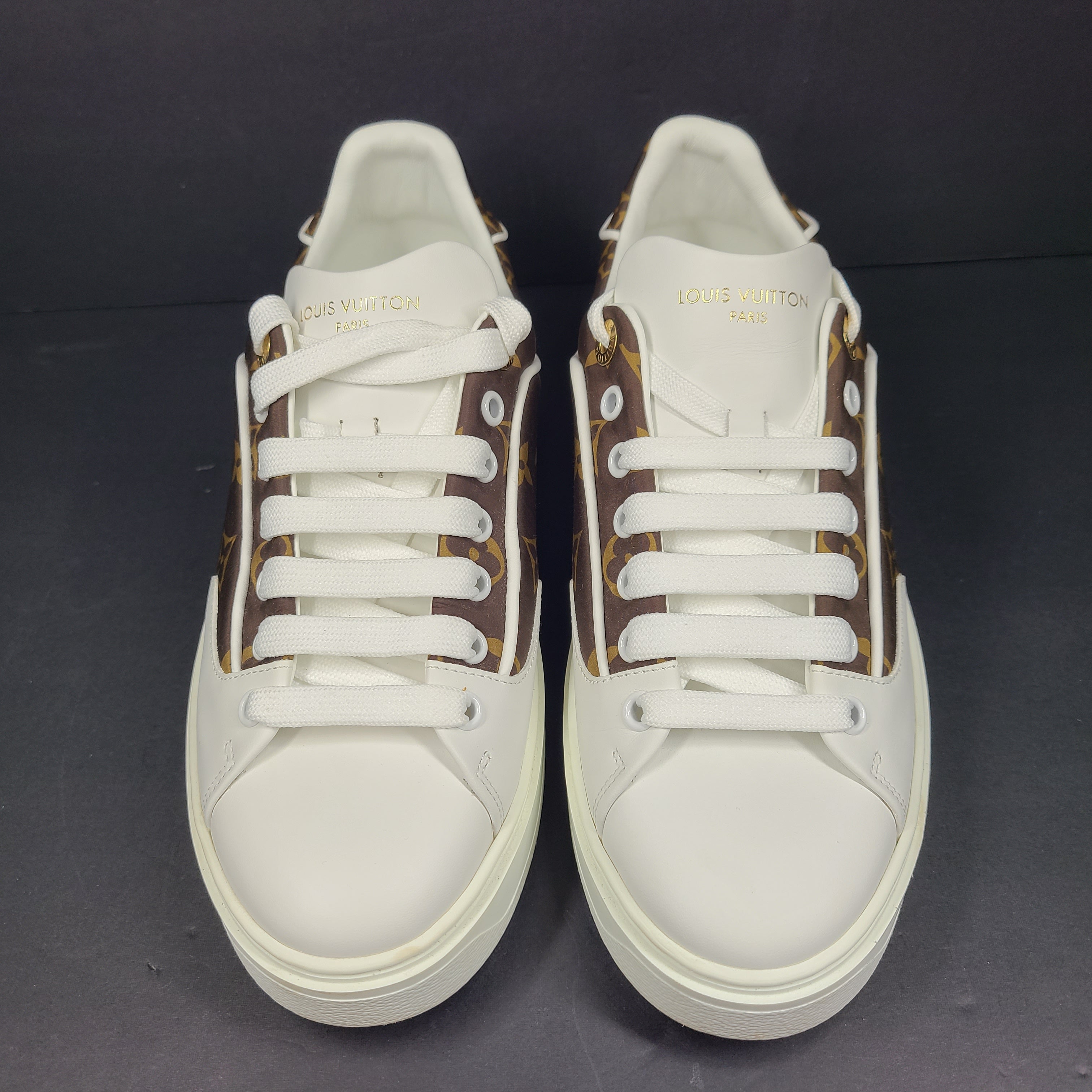 A pair of Louis Vuitton LV Monogram sneakers in white and brown.