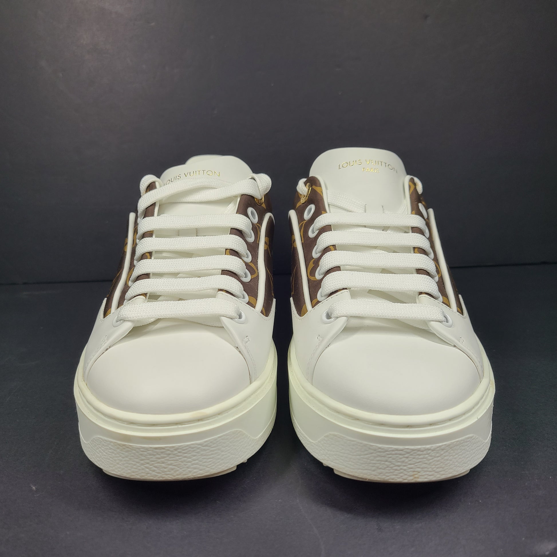 A pair of Louis Vuitton LV Monogram sneakers in white and brown.