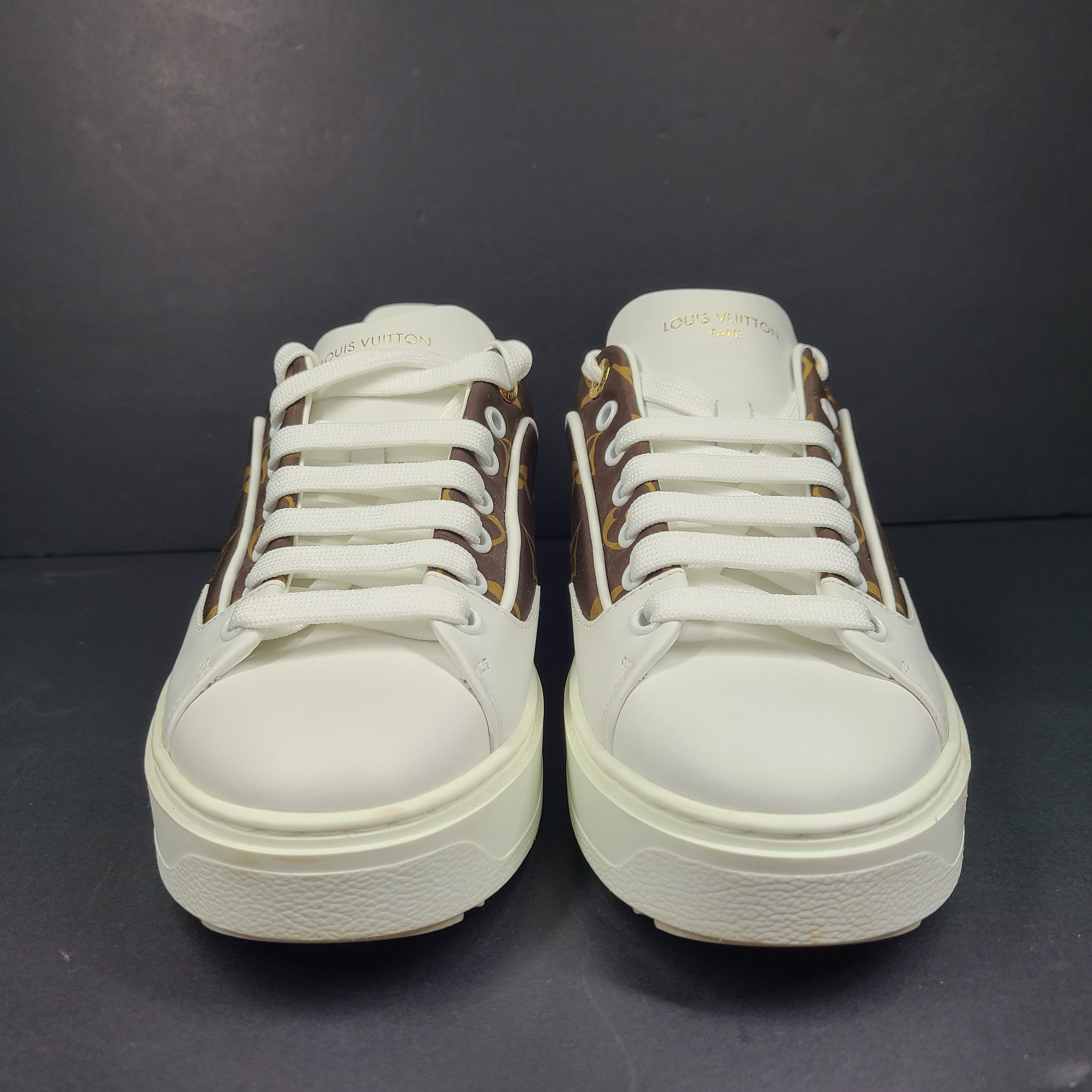 A pair of Louis Vuitton LV Monogram sneakers in white and brown.
