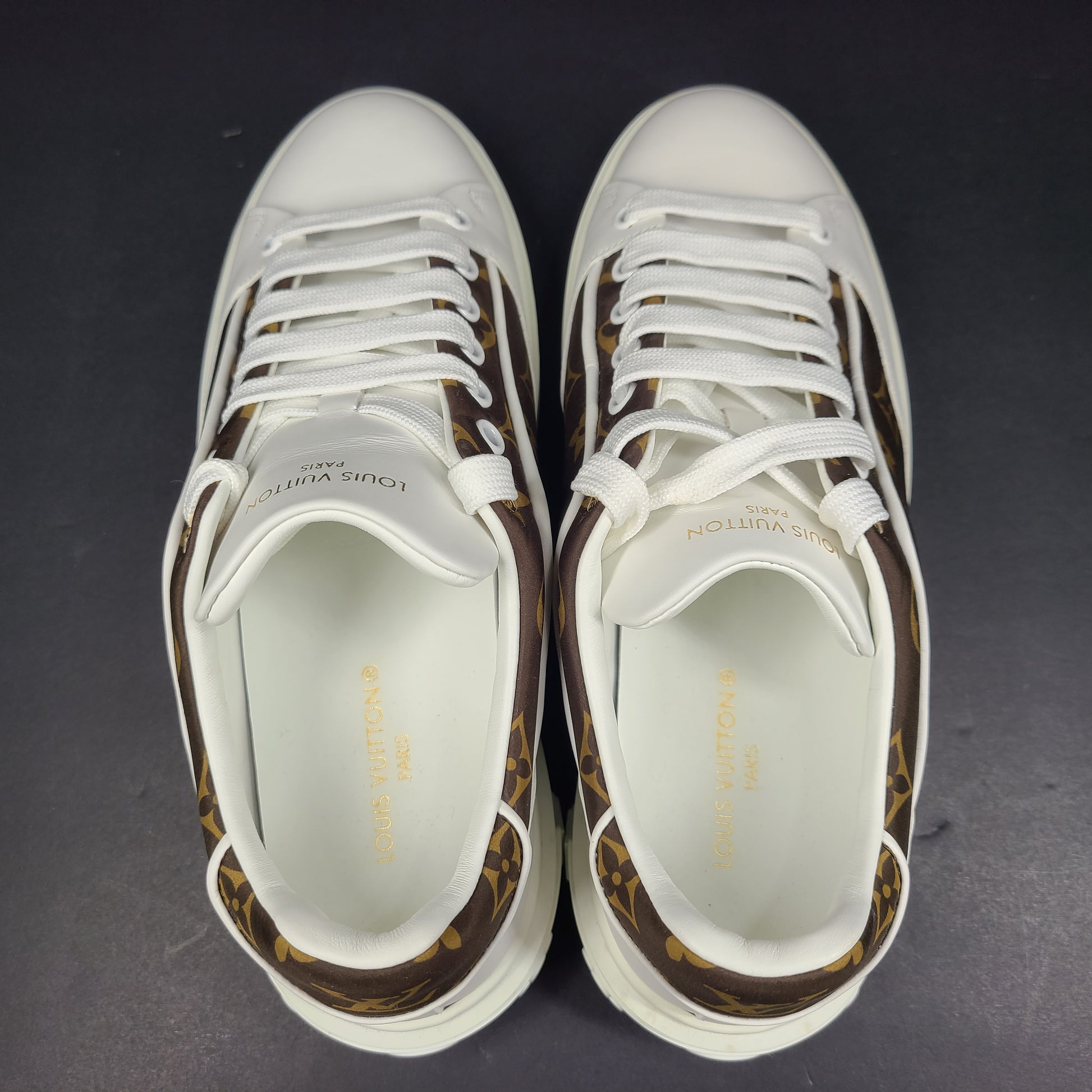 A pair of Louis Vuitton LV Monogram sneakers in white and brown.