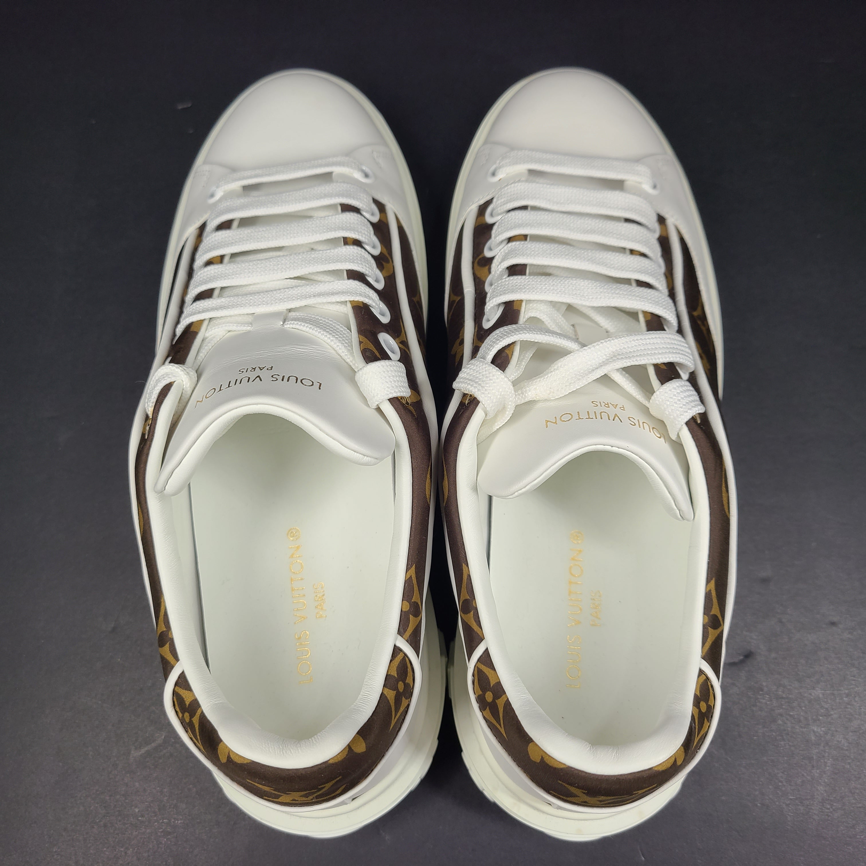 A pair of Louis Vuitton LV Monogram sneakers in white and brown.