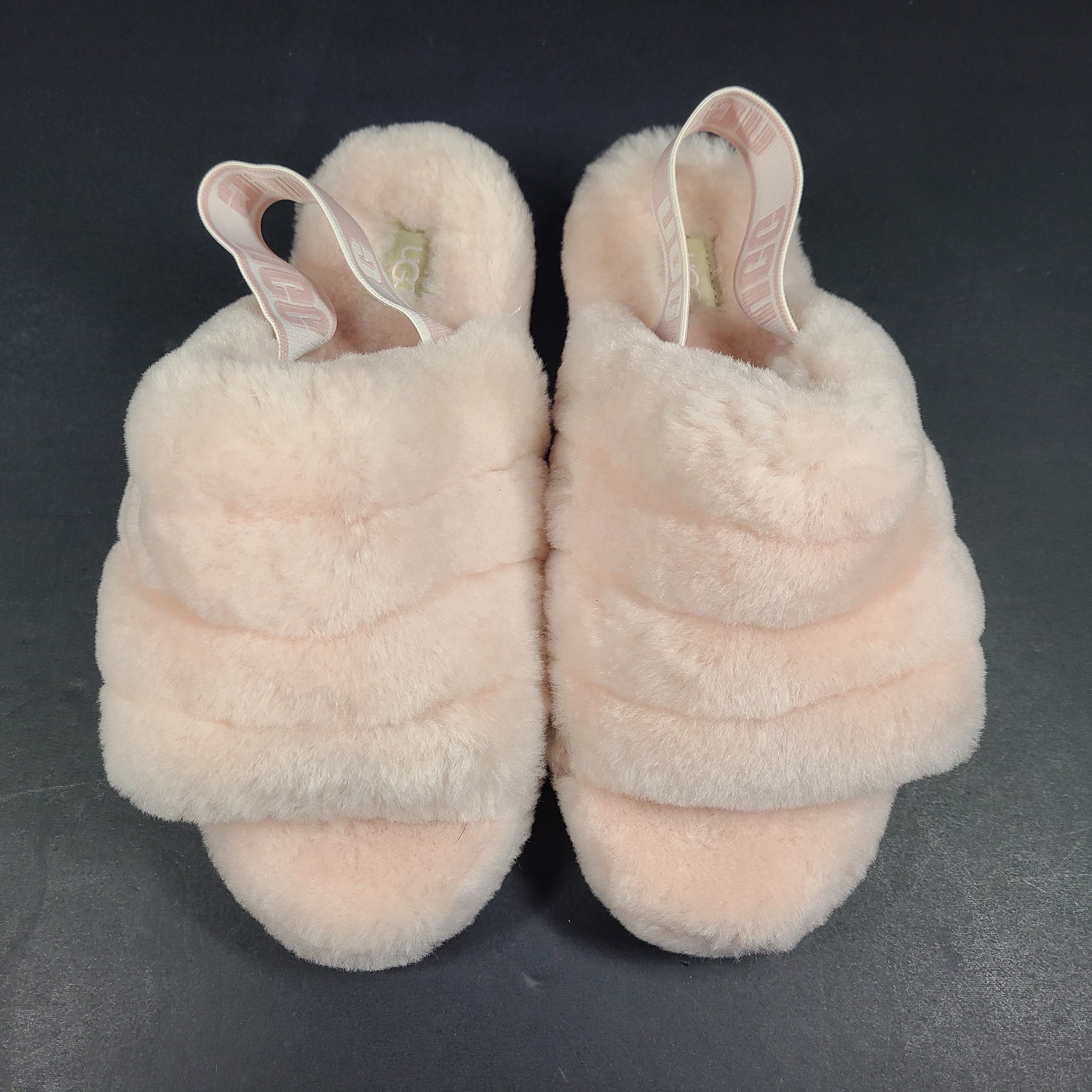 A pair of fluffy pink UGG slide slippers.