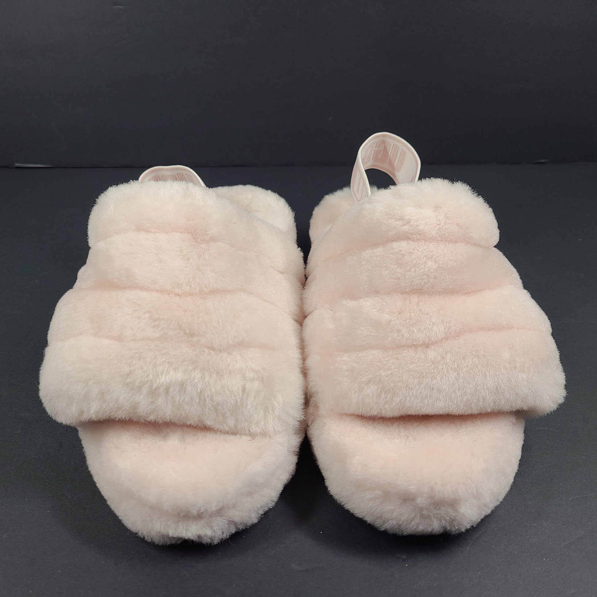 A pair of fluffy pink UGG slide slippers.