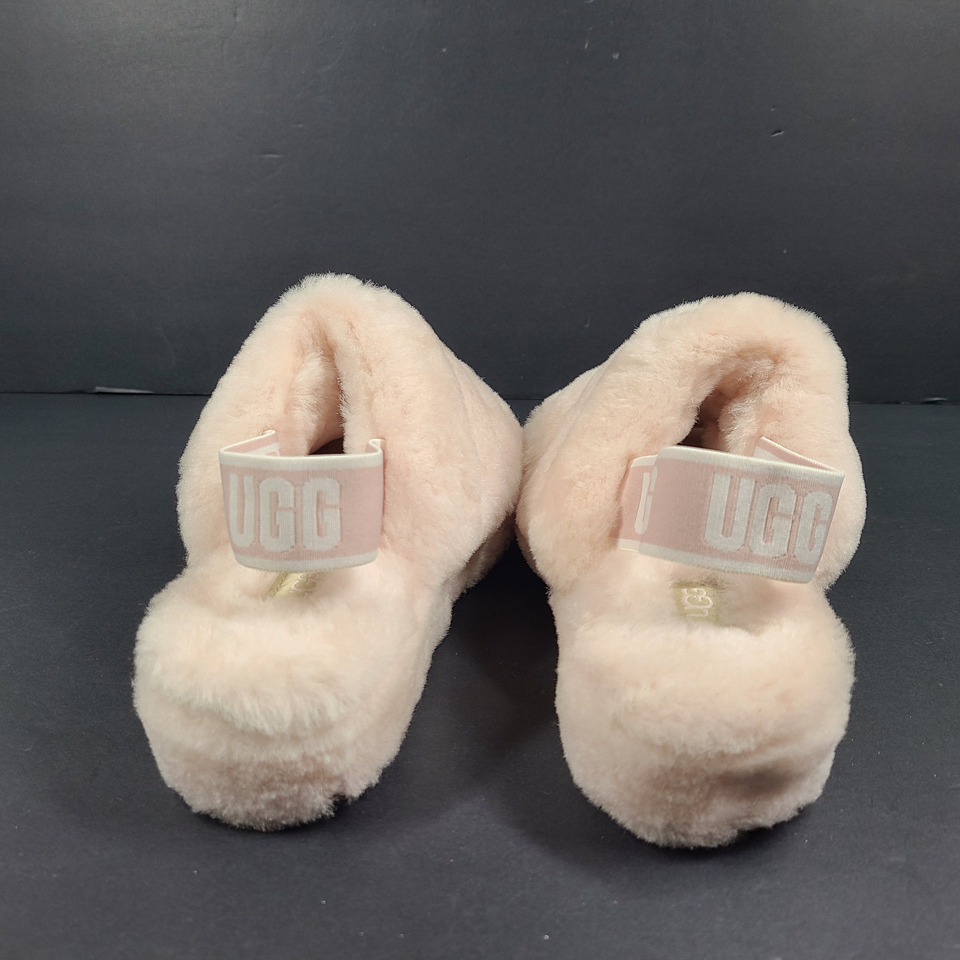 A pair of fluffy pink UGG slide slippers.