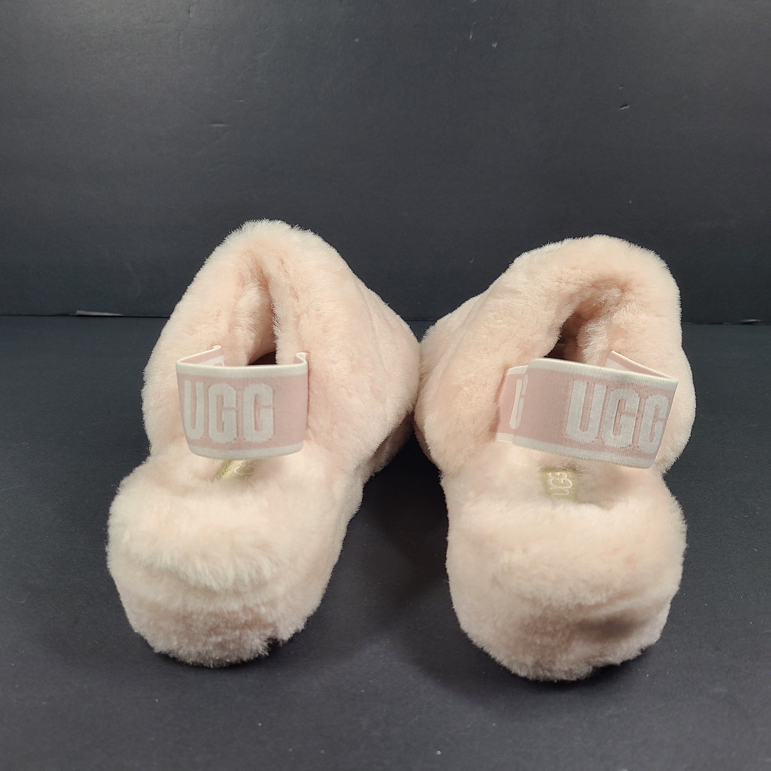 A pair of fluffy pink UGG slide slippers.