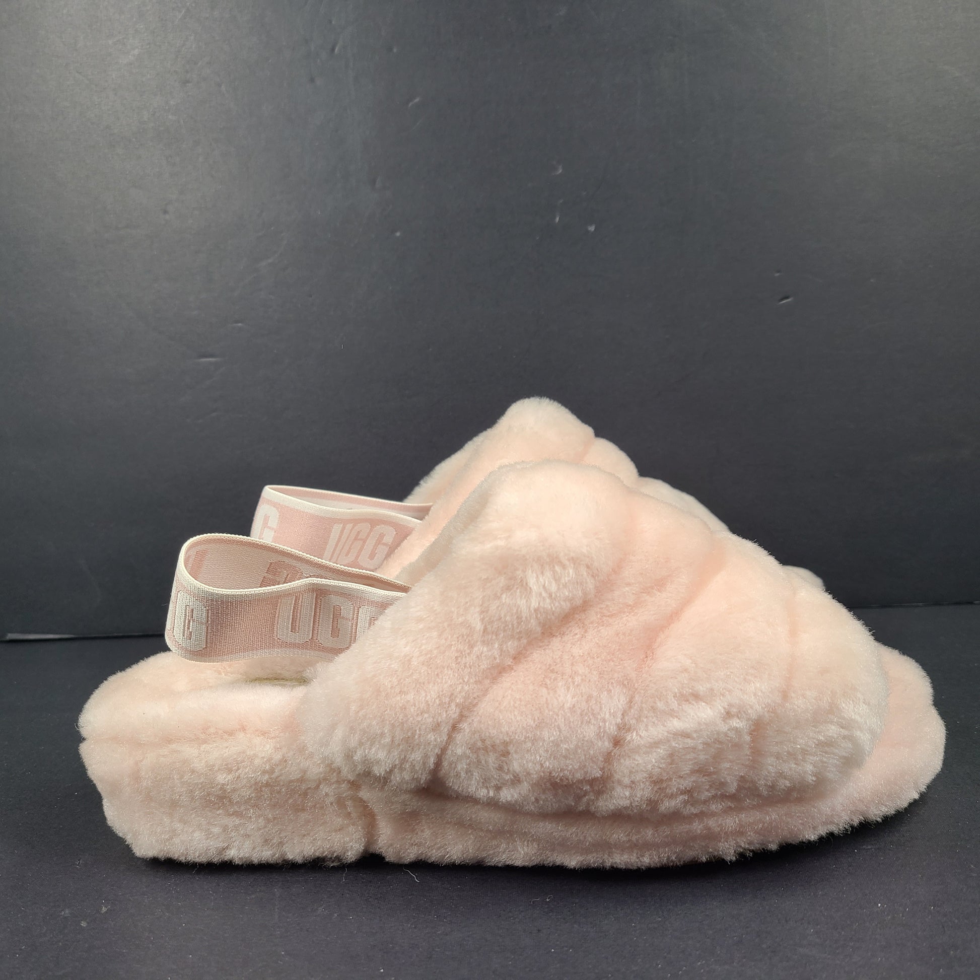 A pair of fluffy pink UGG slide slippers.