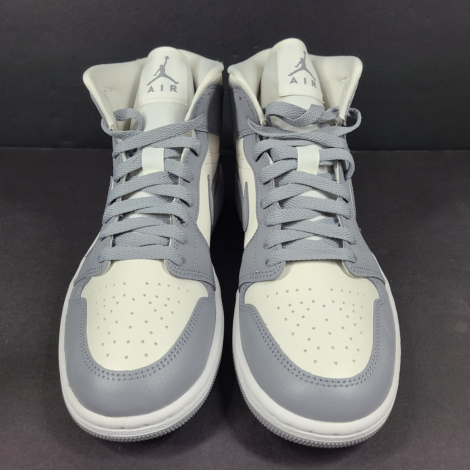 Nike Air Jordan 1 Mid in gray and white with a mid-top profile and classic Swoosh detailing for versatile streetwear styling.