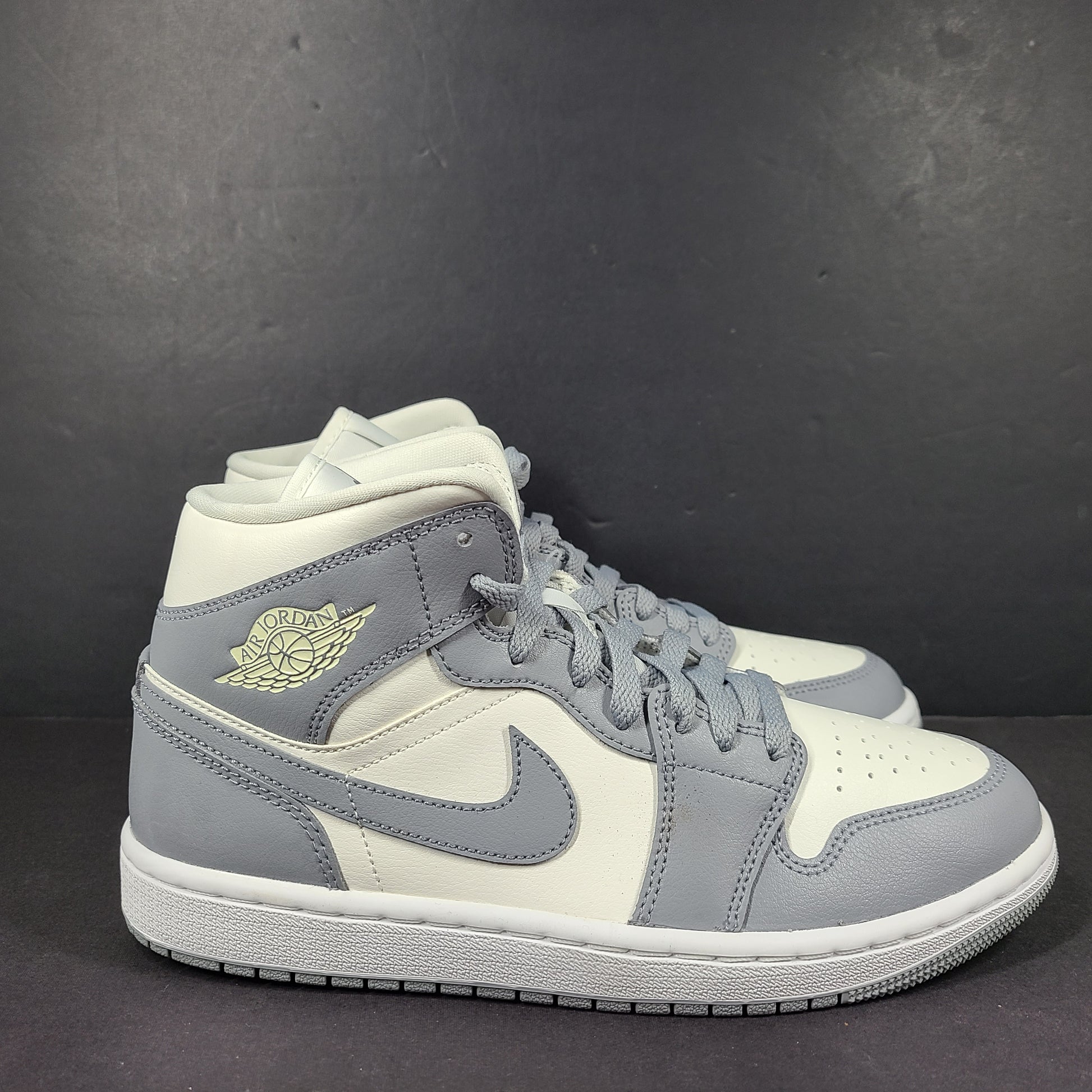 Nike Air Jordan 1 Mid in gray and white with a mid-top profile and classic Swoosh detailing for versatile streetwear styling.
