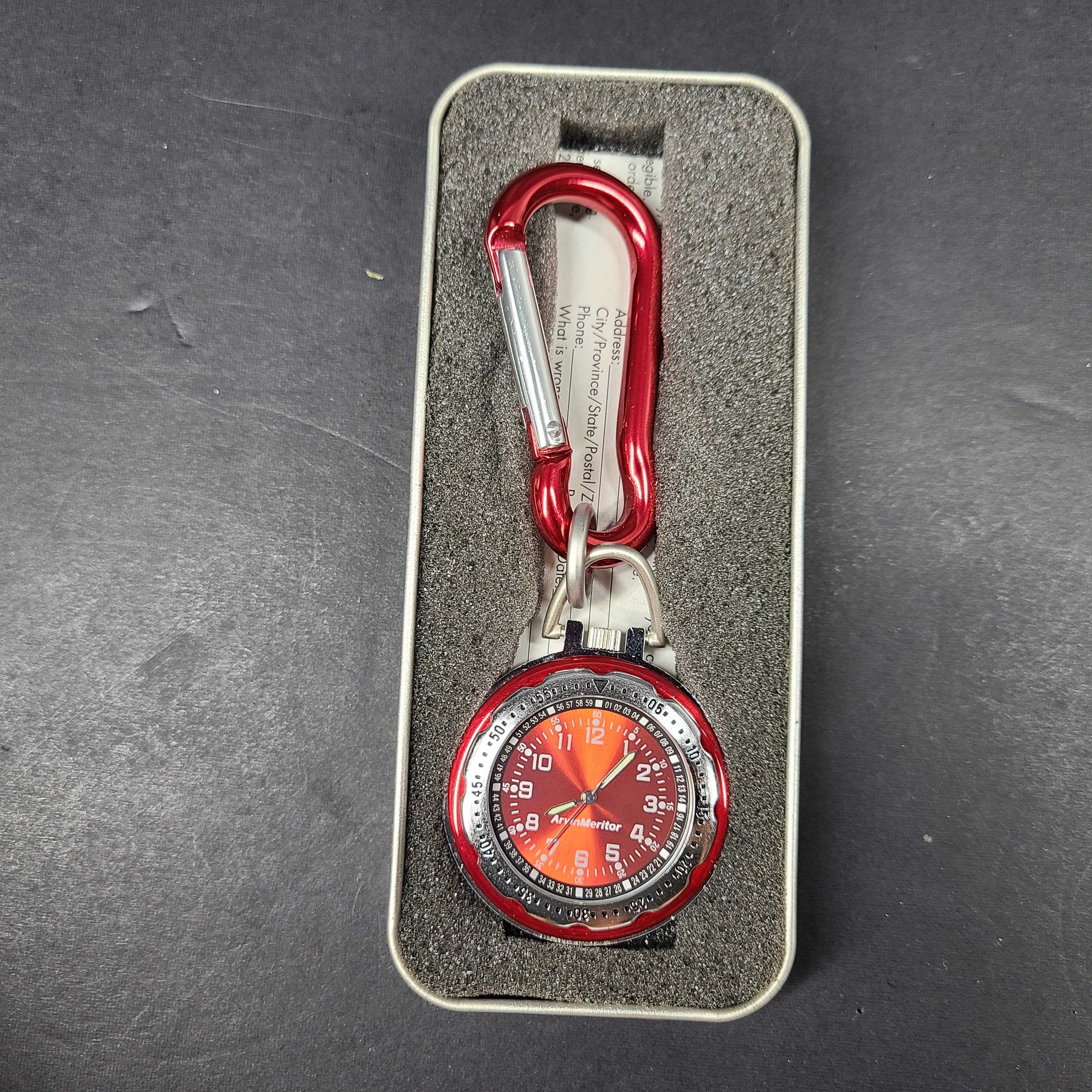 Red and silver pocket watch with a secure carabiner clip, slim profile, and durable construction for active use.