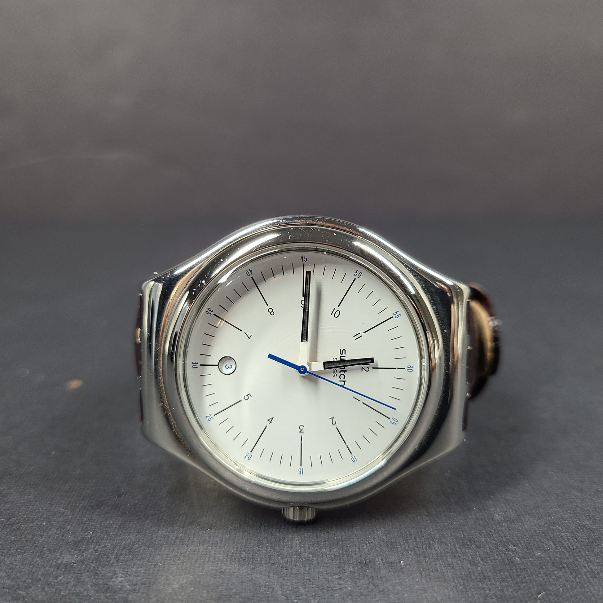 Swatch YGS452G stainless steel wristwatch with a white dial and brown leather strap.