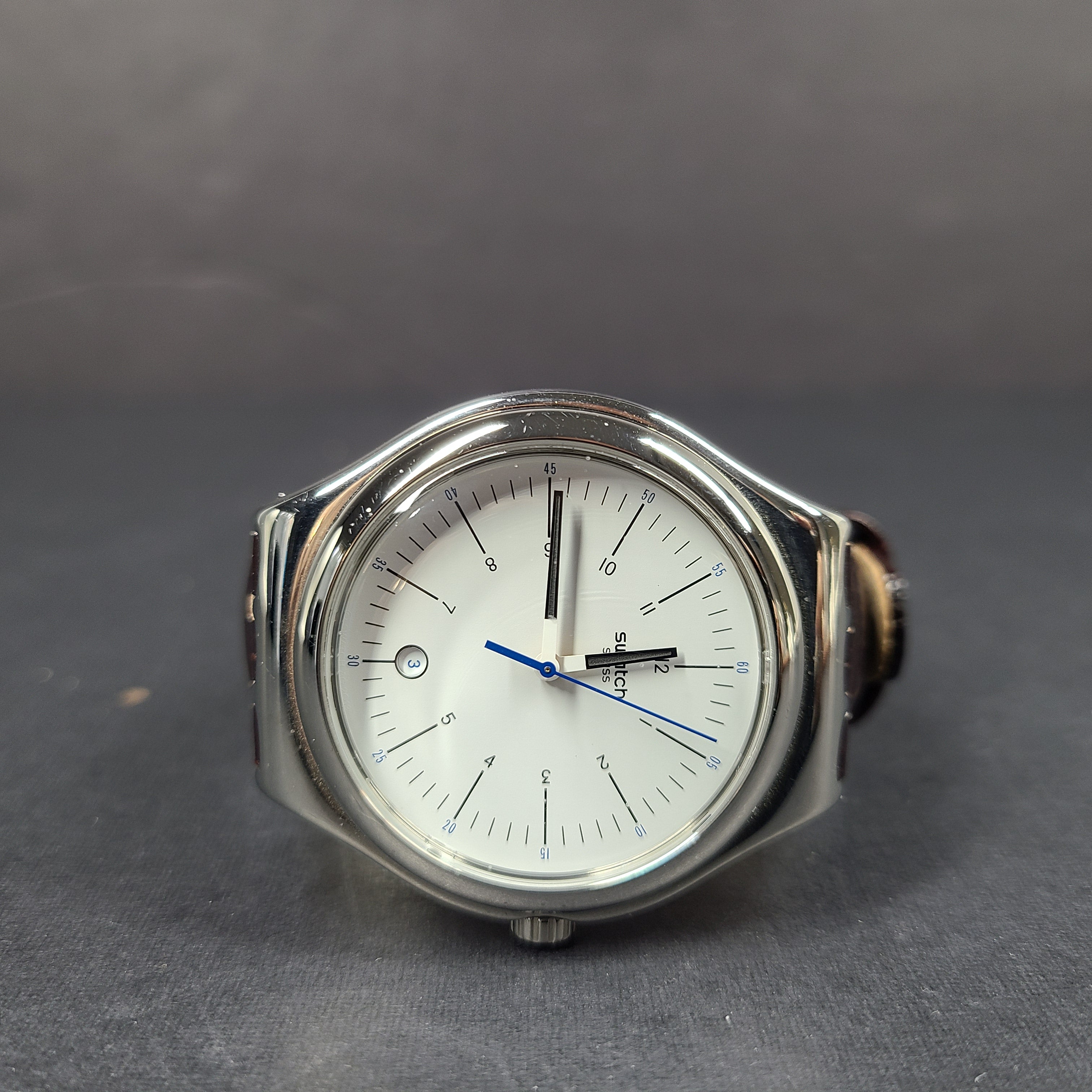 Swatch YGS452G stainless steel wristwatch with a white dial and brown leather strap.