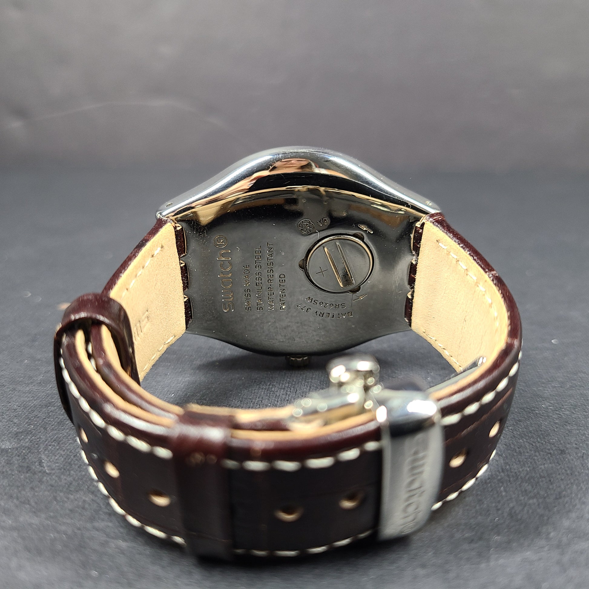 Swatch YGS452G stainless steel wristwatch with a white dial and brown leather strap.