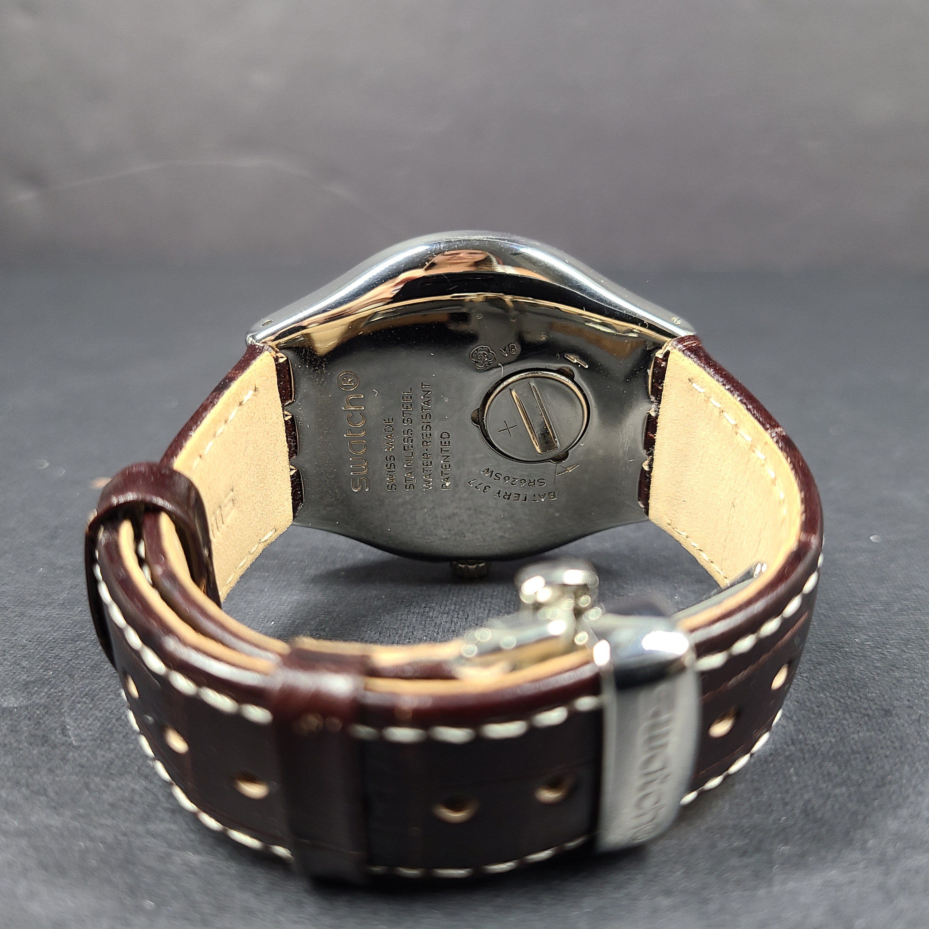 Swatch YGS452G stainless steel wristwatch with a white dial and brown leather strap.