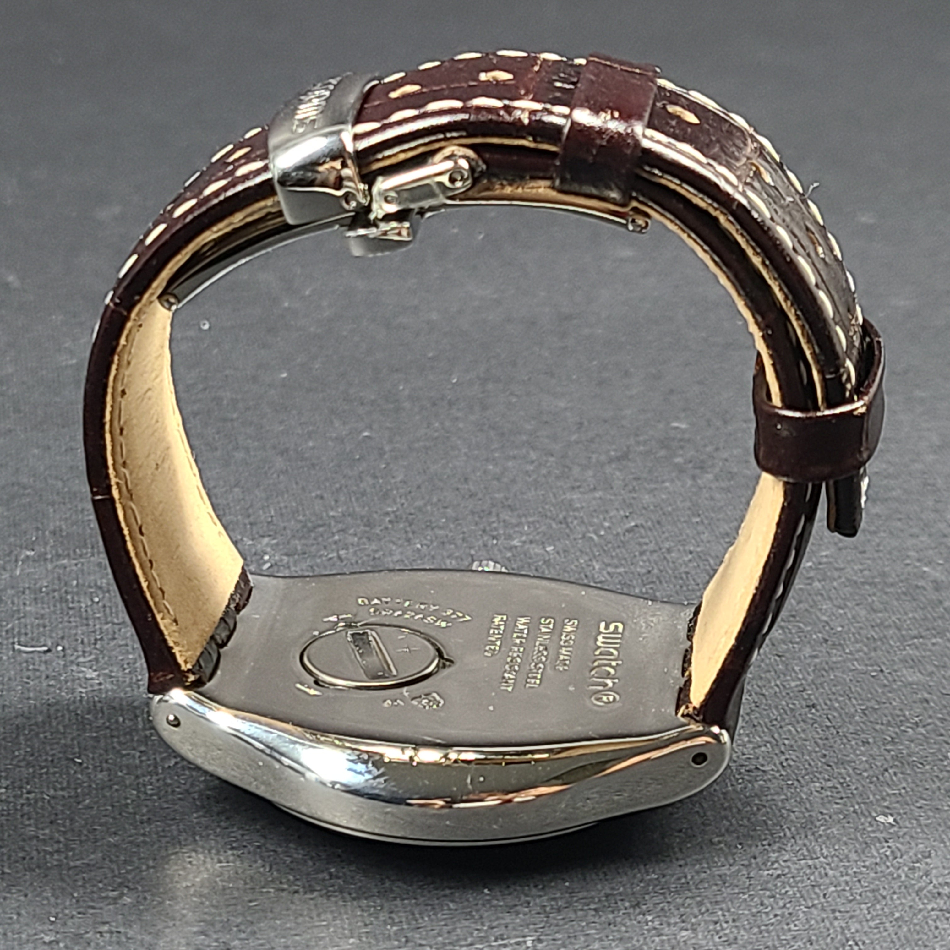 Swatch YGS452G stainless steel wristwatch with a white dial and brown leather strap.
