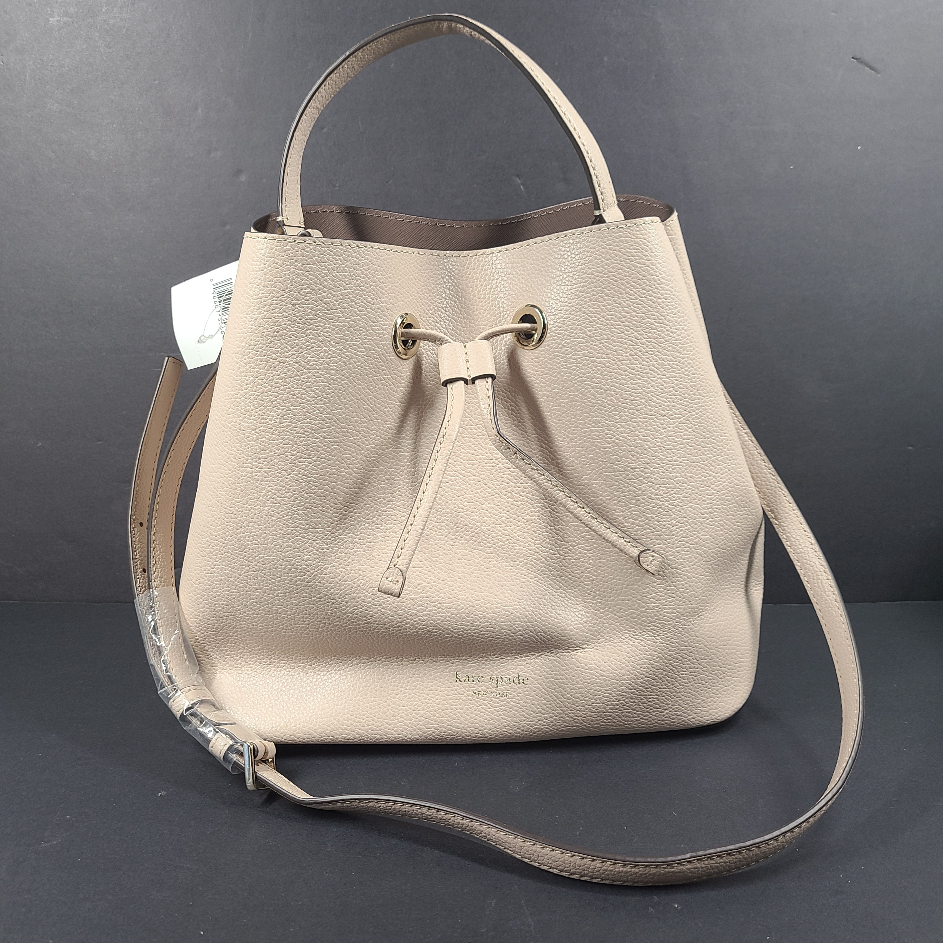 Beige Kate Spade handbag with intact price tag and protective plastic on the straps.