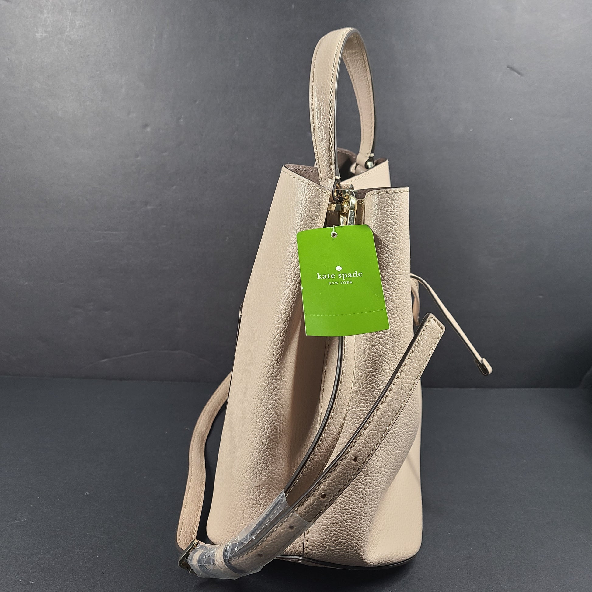 Beige Kate Spade handbag with intact price tag and protective plastic on the straps.