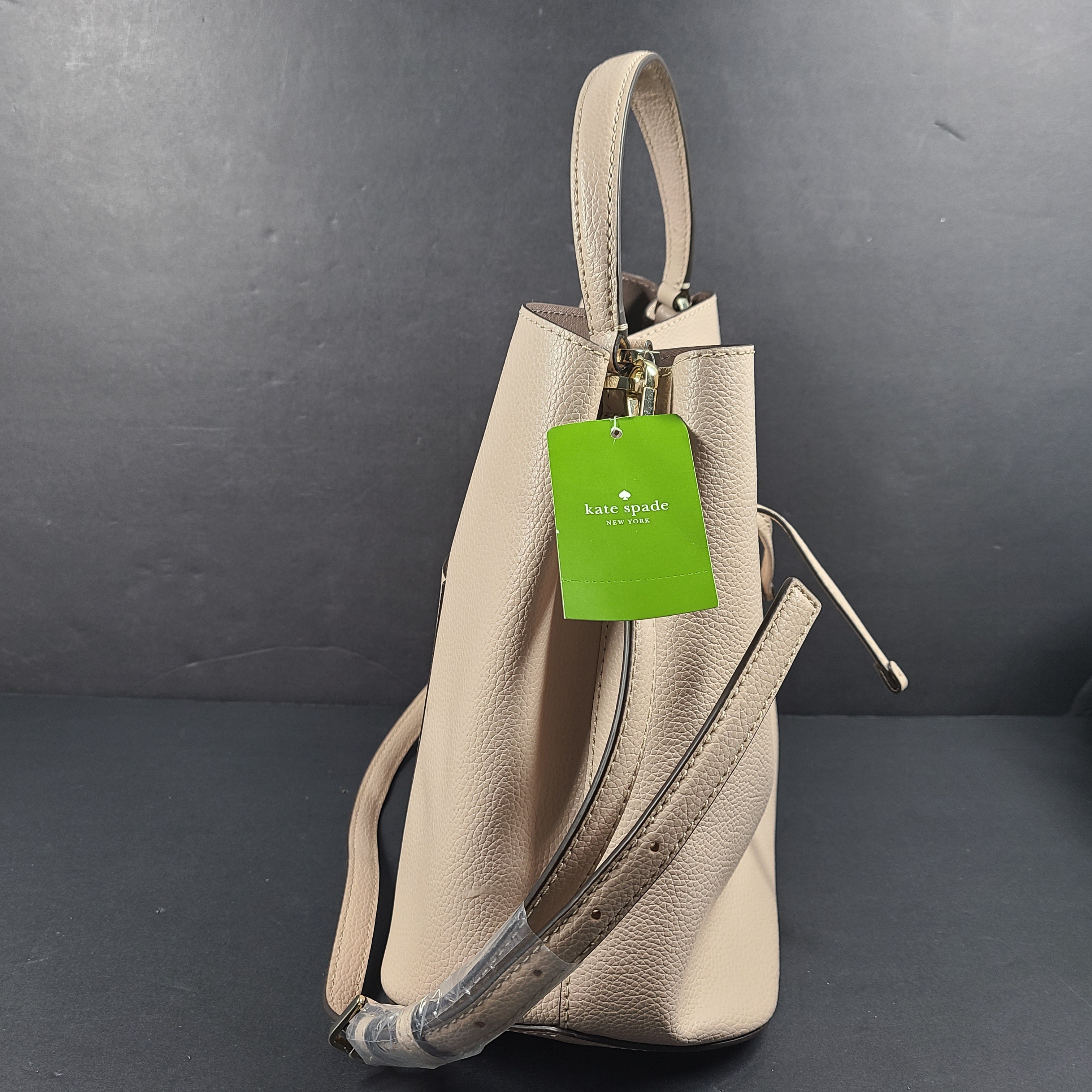 Beige Kate Spade handbag with intact price tag and protective plastic on the straps.