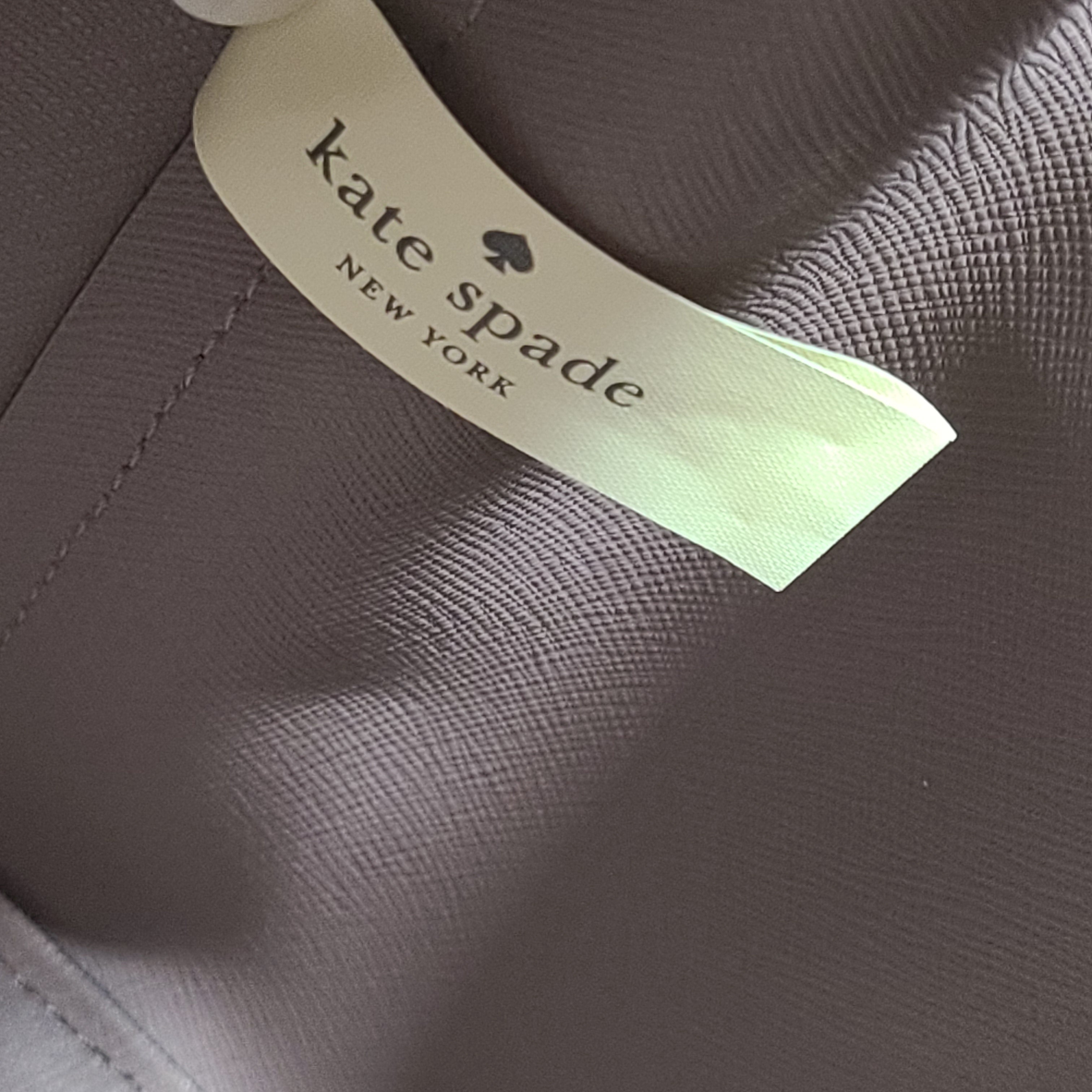 Beige Kate Spade handbag with intact price tag and protective plastic on the straps.