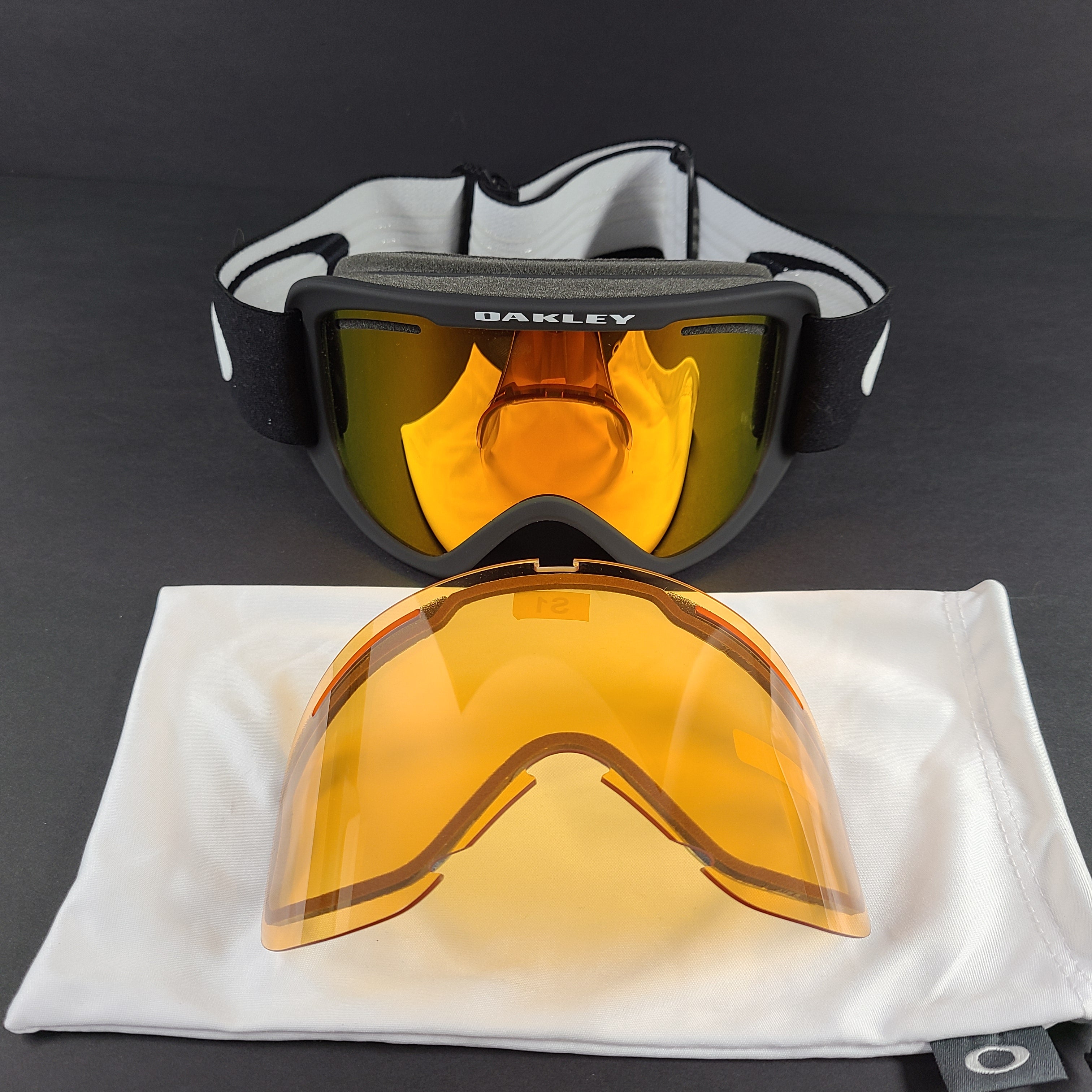 Oakley black snow goggles feature an orange lens and include an extra replacement lens and storage bag.