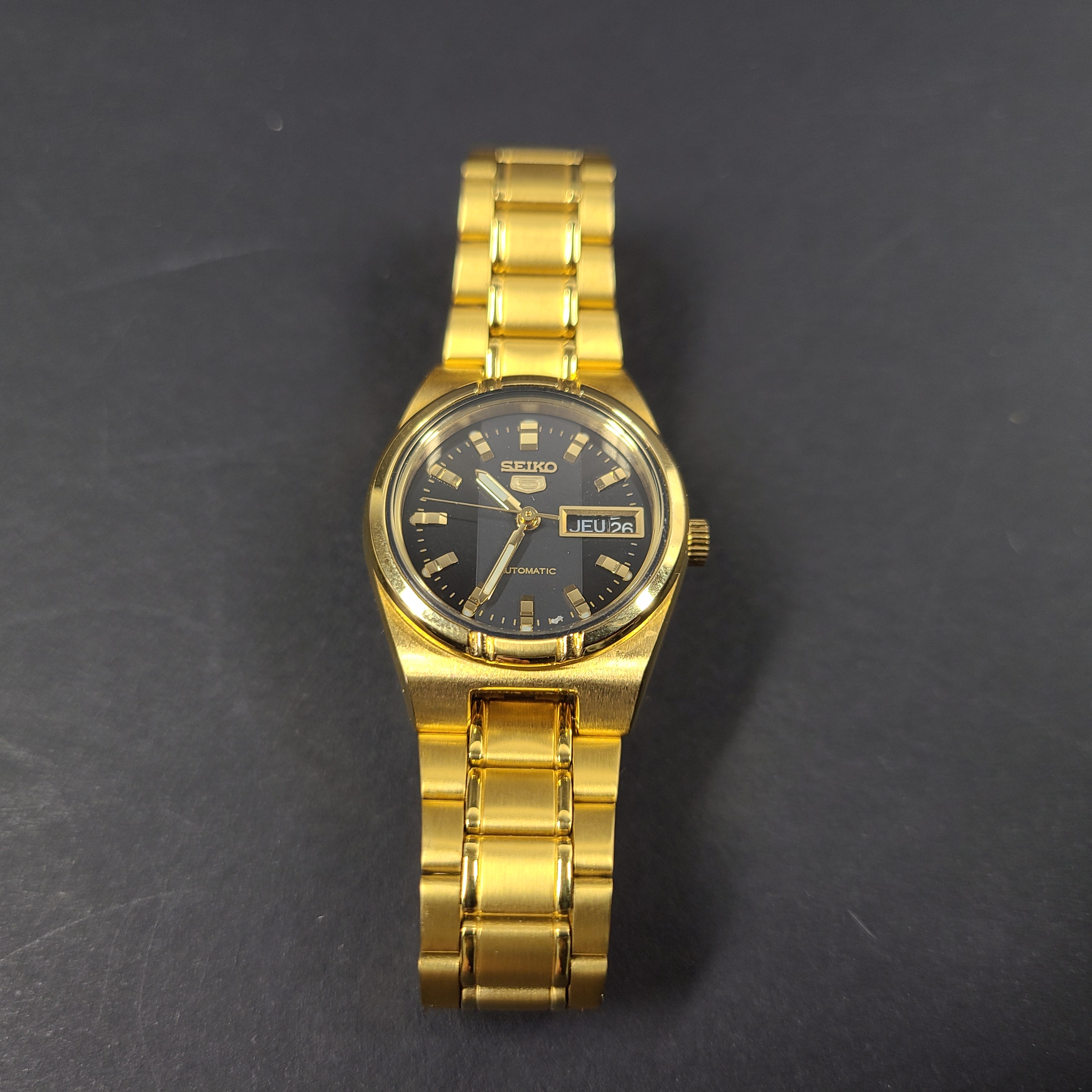 Gold-tone Seiko 5 automatic ladies watch with a black dial and stainless steel bracelet.